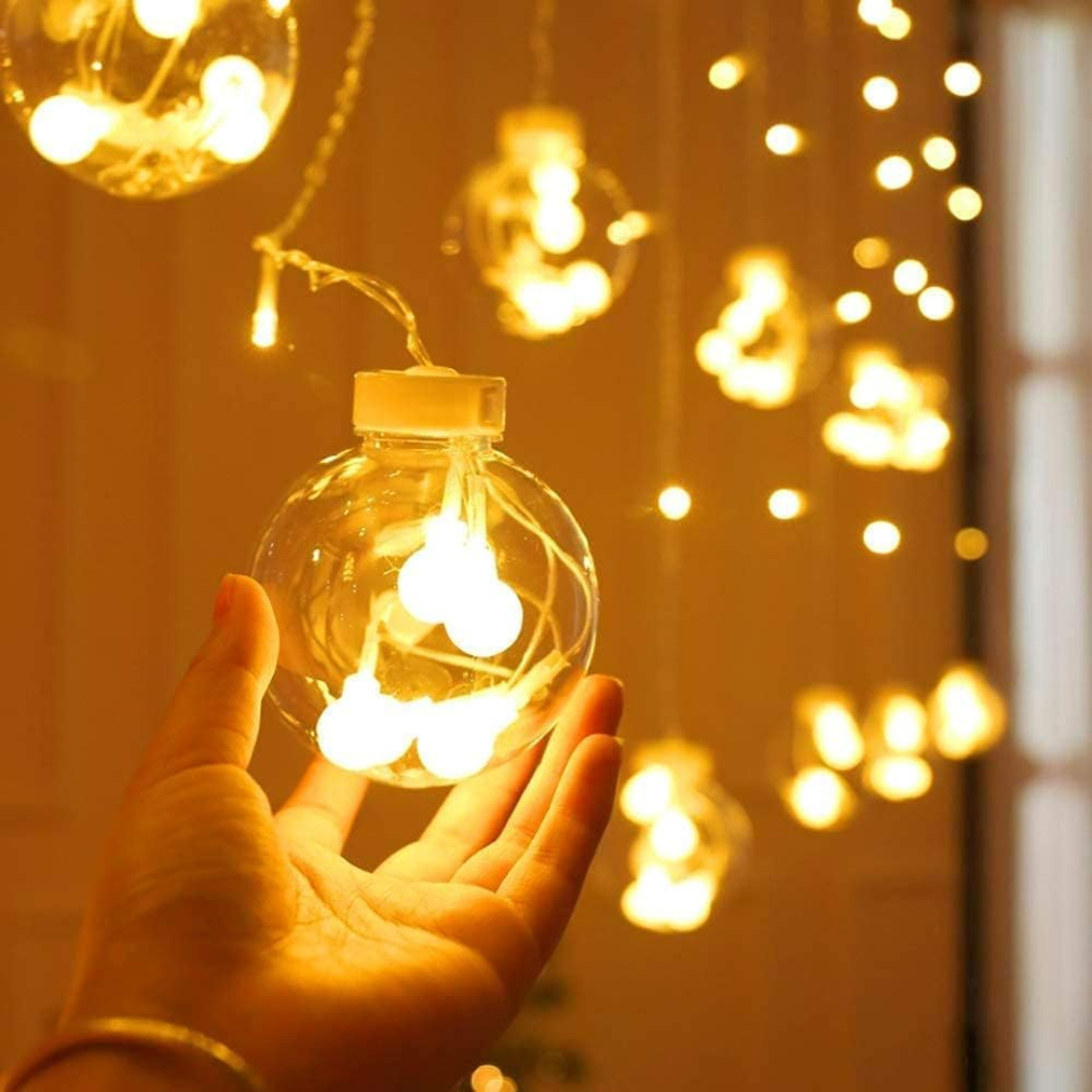 Hand holding a clear glass ornament with string lights against a warm glow background