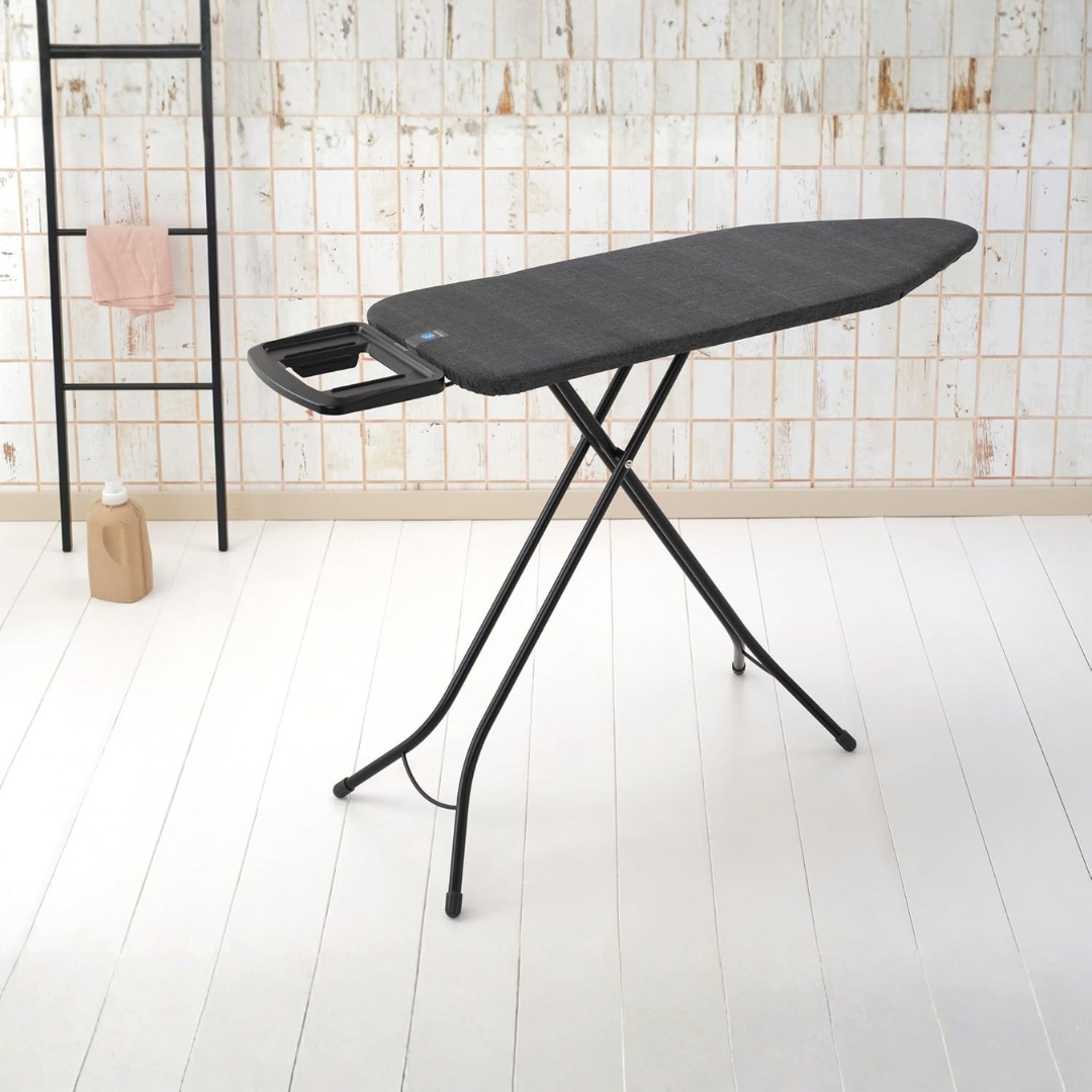 Black ironing board with a handle on a white floor against a tiled wall.