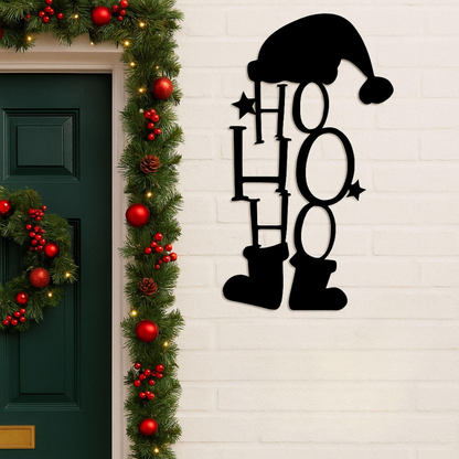 Decorative metal sign with 'HO HO HO' text, Santa hat, and boots on a white brick wall with Christmas decorations.