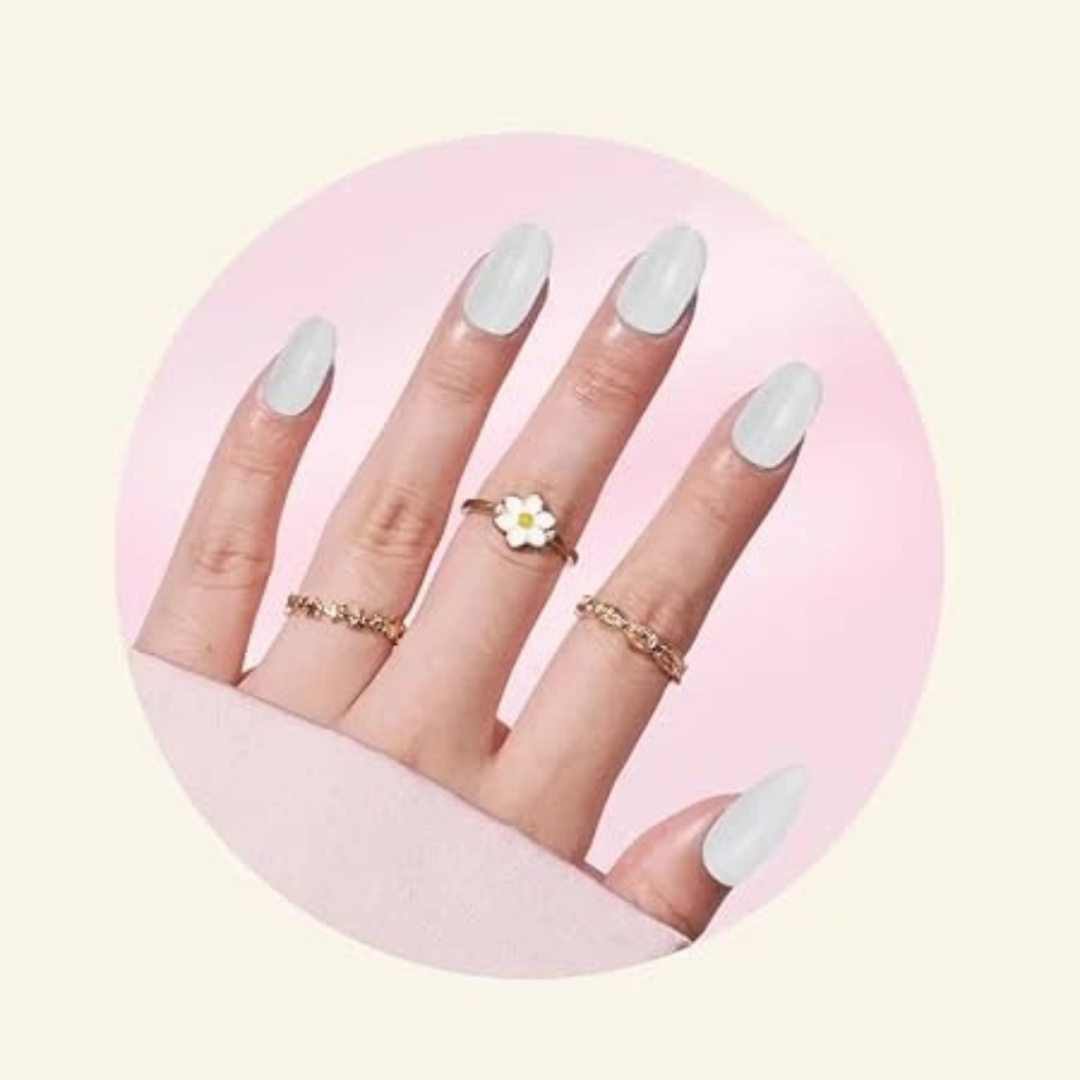 Hand with light gray nail polish wearing gold rings on a pink background